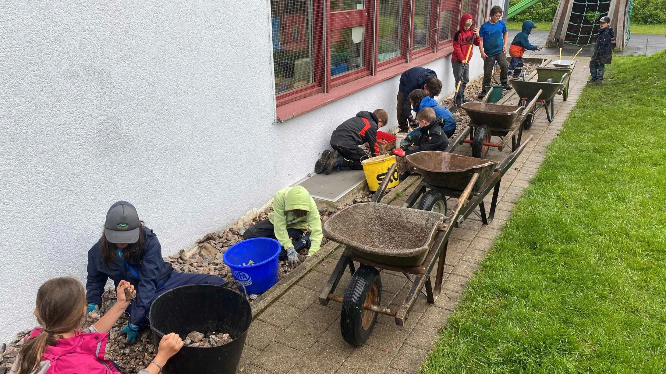 Schüler:innen der Gemeinde Kallern entfernen Steine aus der Rabatte beim Schulhaus im Mai 2024